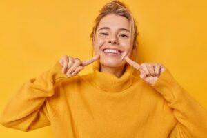 Happy young woman in yellow sweater pointing at her teeth